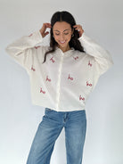 Woman wearing a white cardigan with red 'ho ho ho' text and blue jeans on a white background