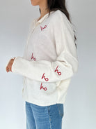 White sweater with red 'ho ho ho' text worn by a person on a white background from side