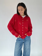 Woman wearing a red cardigan with 'ho ho ho' gold embroidered text and blue jeans on a white background
