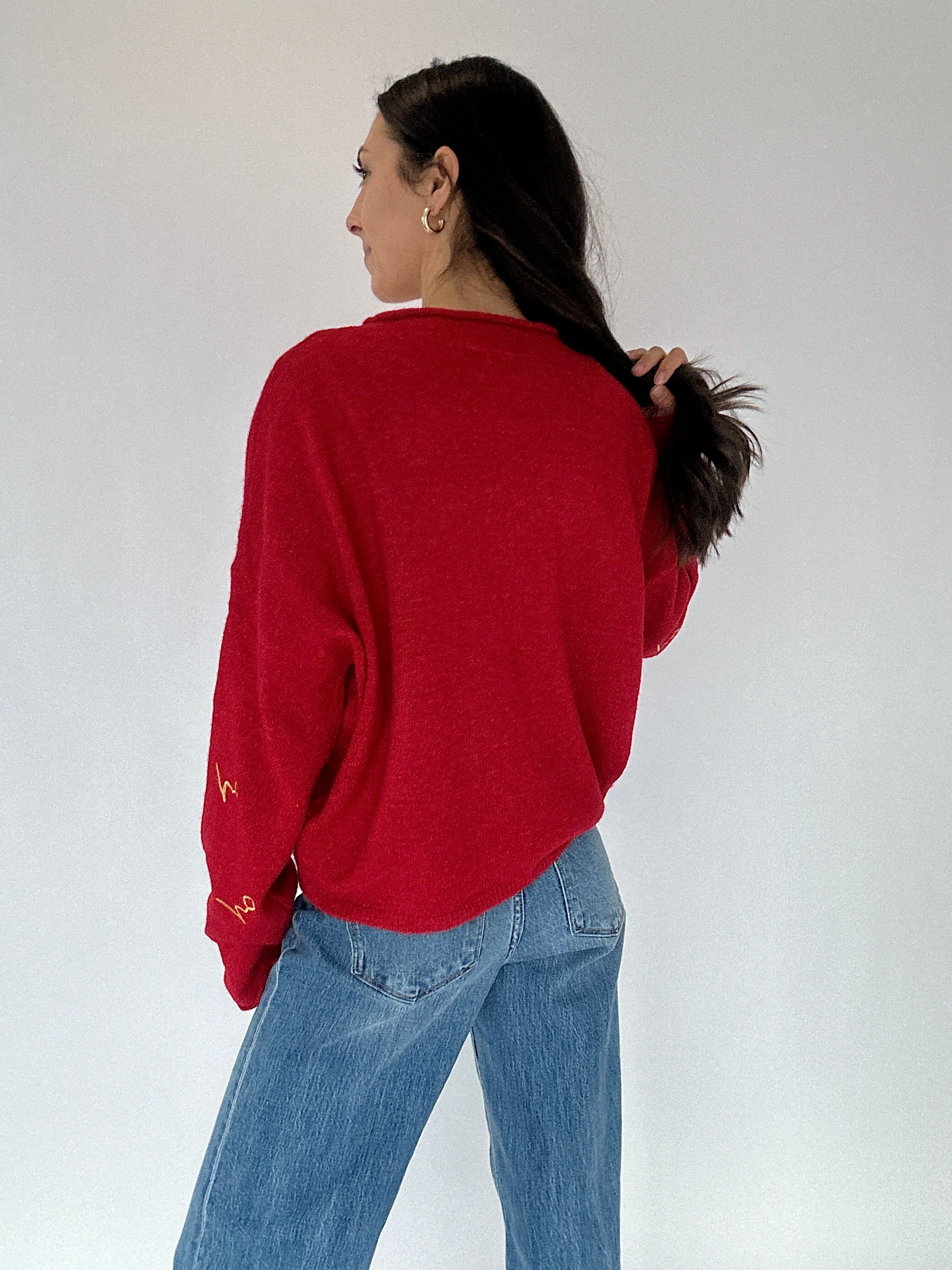 Person wearing a red sweater from back and blue jeans against a white background