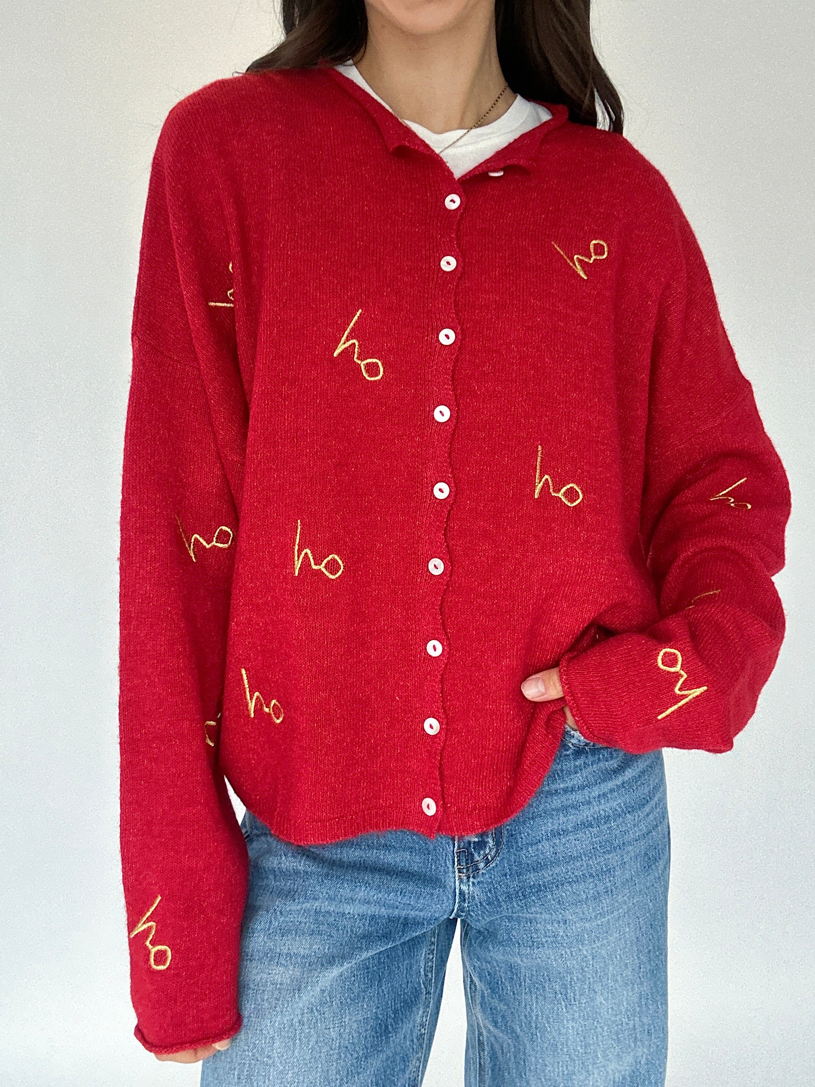 Red cardigan with 'ho ho ho' gold embroidered patterns worn by a person on a white background