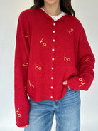Red cardigan with 'ho ho ho' gold embroidered patterns worn by a person on a white background