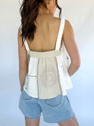Woman wearing a sleeveless top with a crochet pattern and denim shorts against a light background showing the back elastic