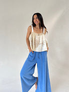 A woman modeling a cream sleeveless top with crochet detailing and wide-leg blue jeans against a plain light gray studio background.