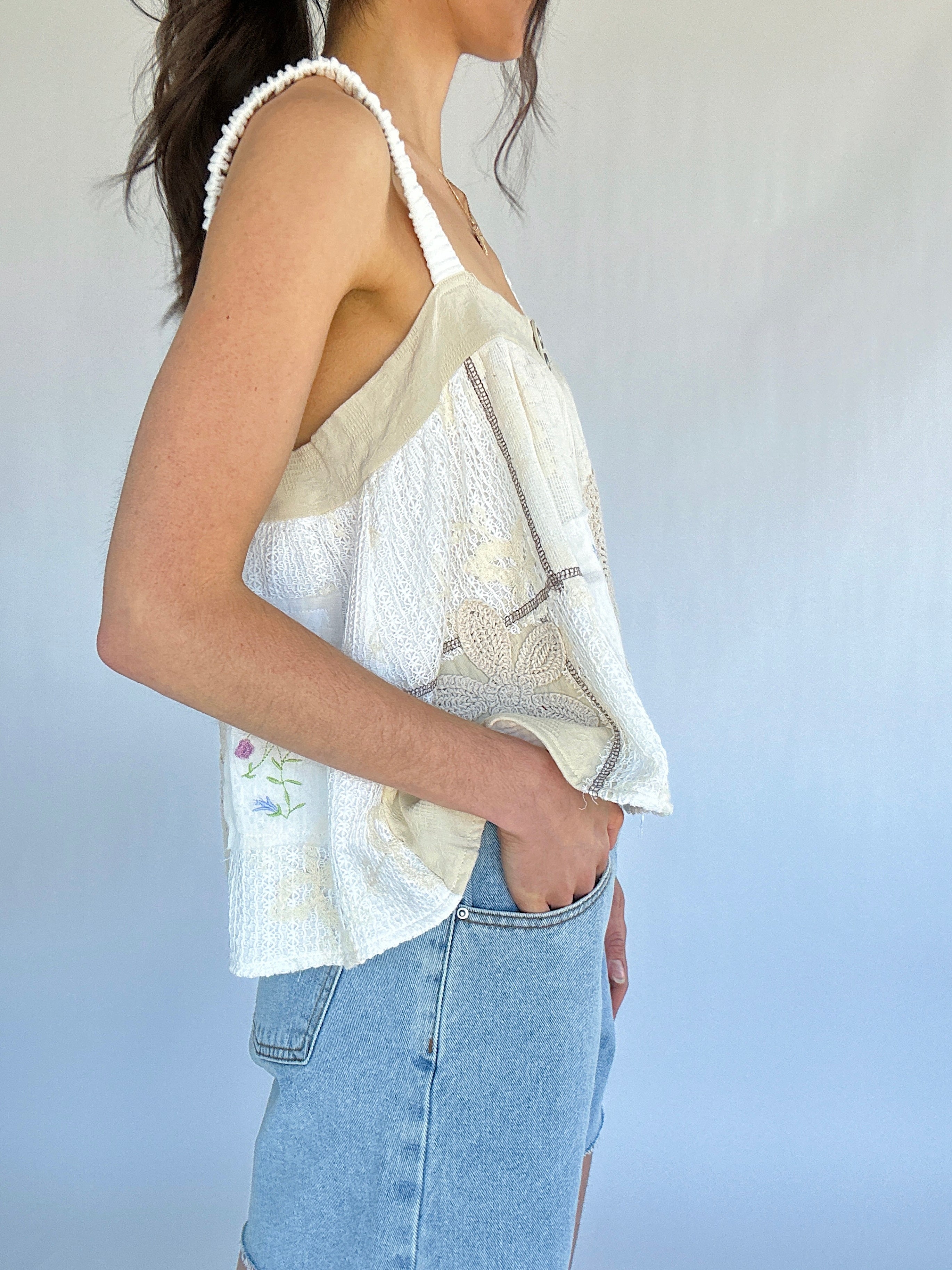 Person wearing a light-colored sleeveless top with floral patterns and light blue jeans against a plain background