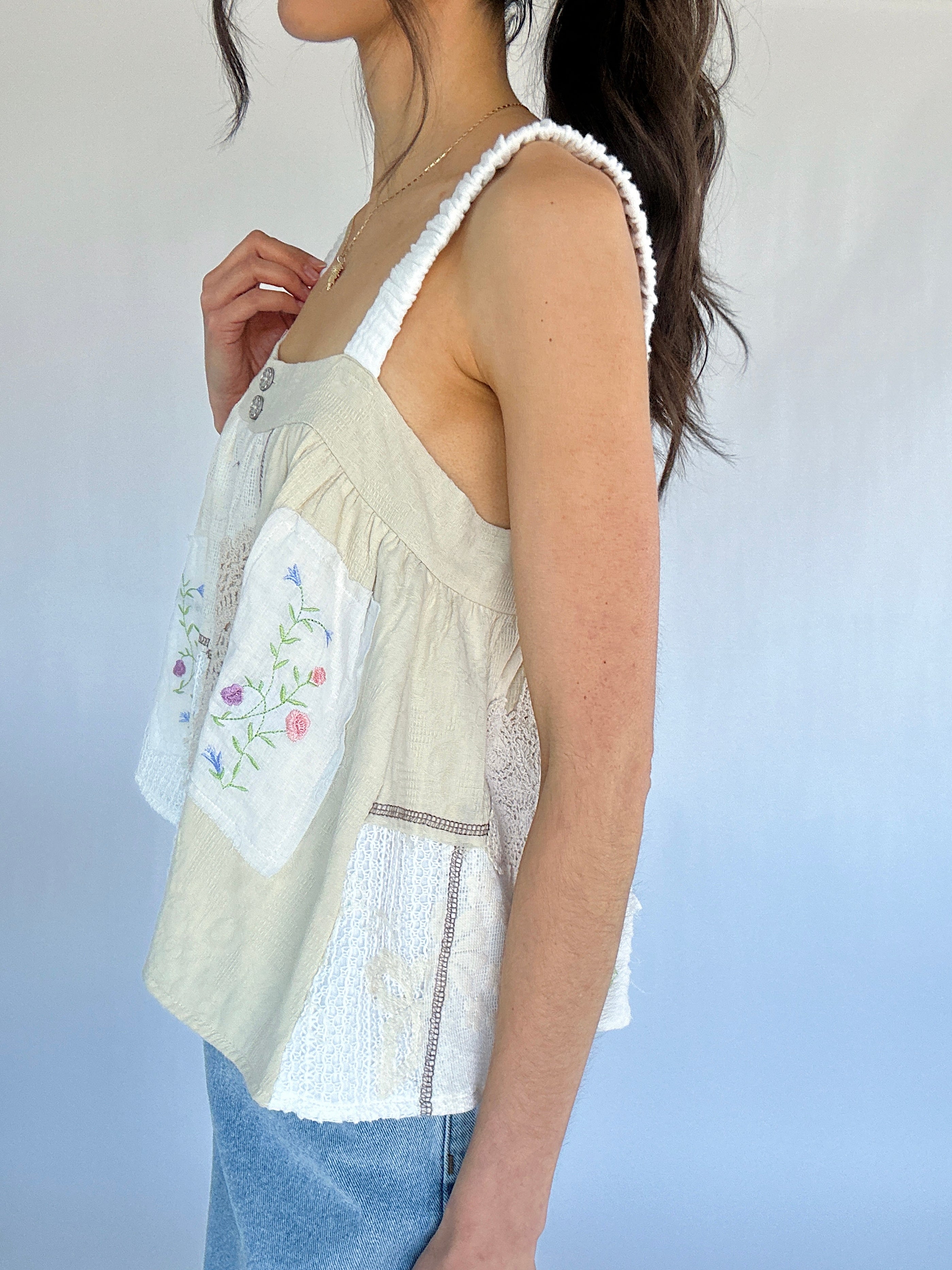 Woman wearing a light-colored sleeveless top with floral embroidery against a plain background from side