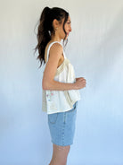 Woman wearing a white sleeveless top and denim shorts against a plain background from side