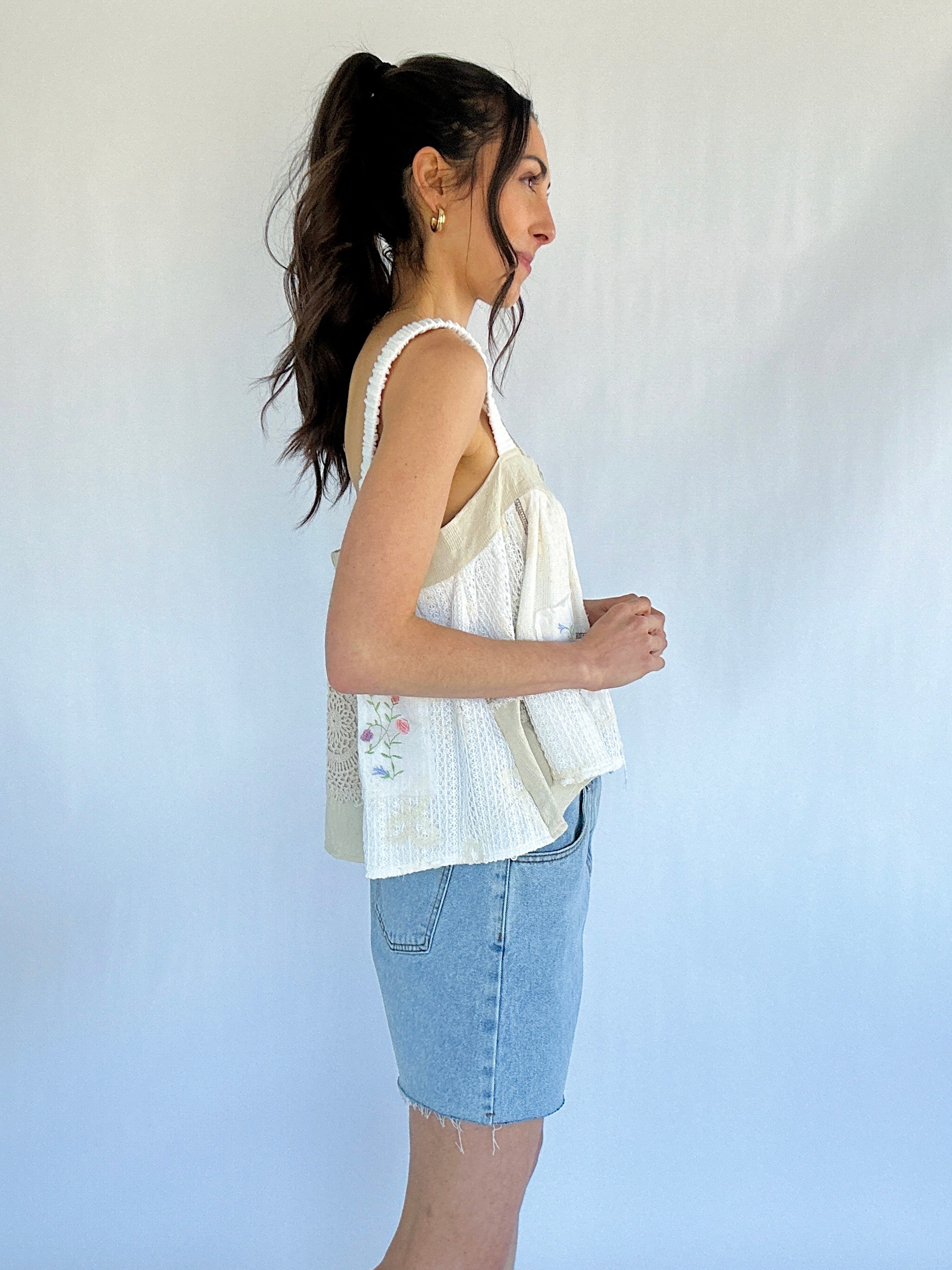 Woman wearing a white sleeveless top and denim shorts against a plain background from side