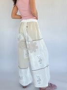 Woman wearing a pink top and beige floral pants on a plain background from back