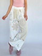 Person wearing a white embroidered pants with floral patterns on a plain background