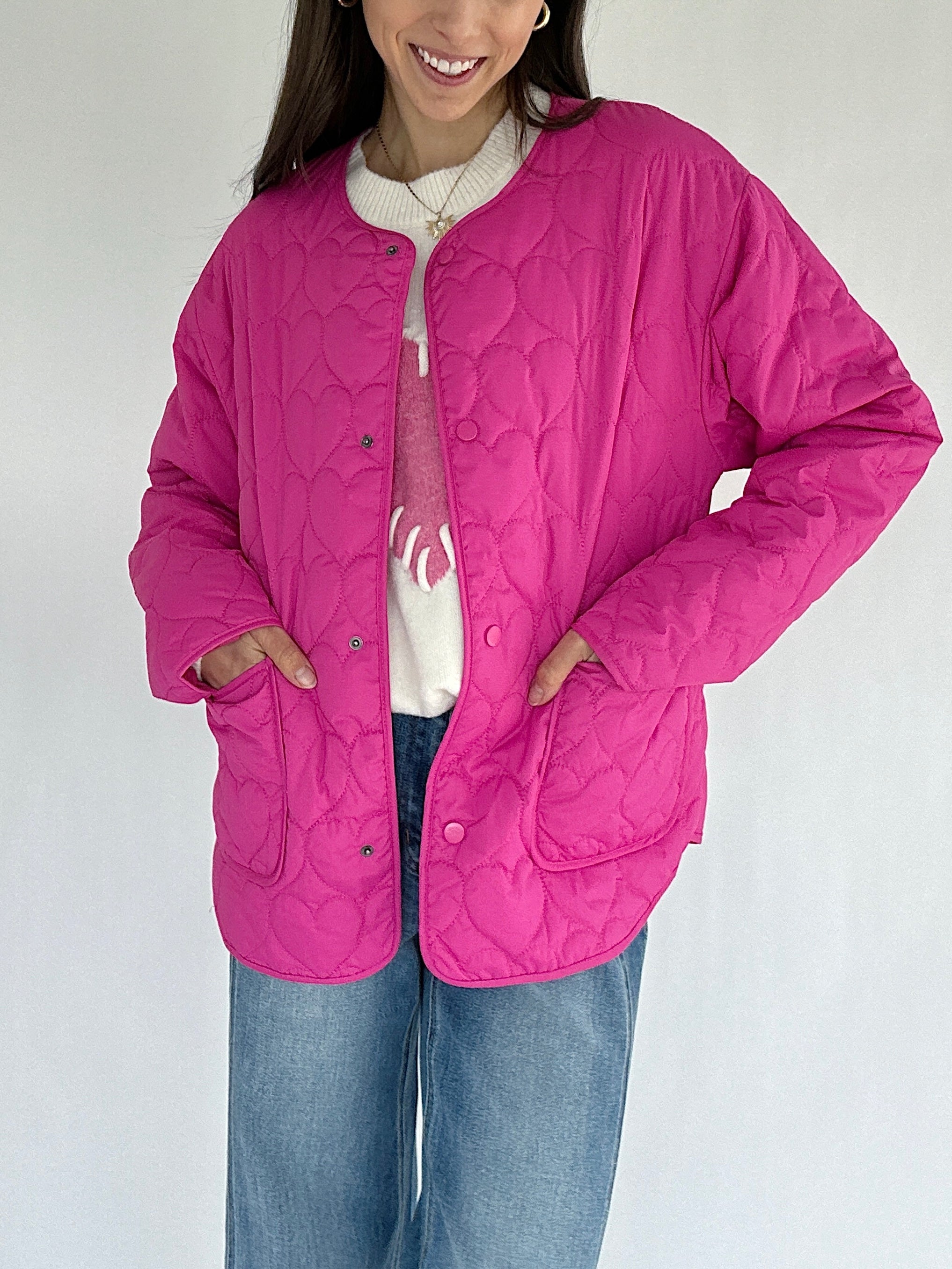 Person wearing a pink quilted jacket on a white background with hands in pockets
