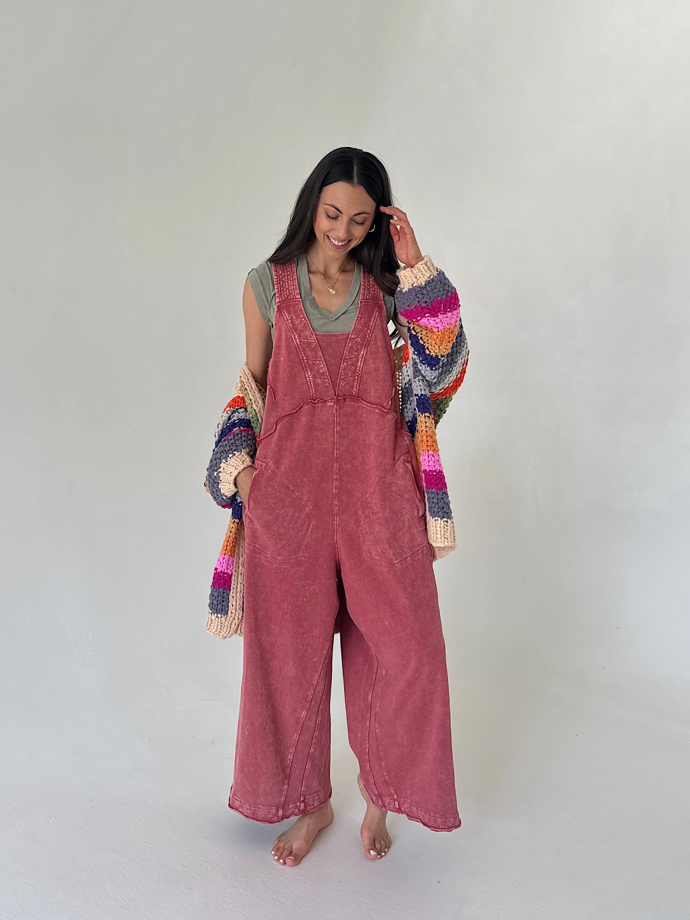 Woman wearing pink overalls with a colorful sweater against a white background