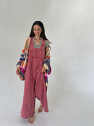 Woman wearing pink terry knit overalls with a colorful cardigan on a white background