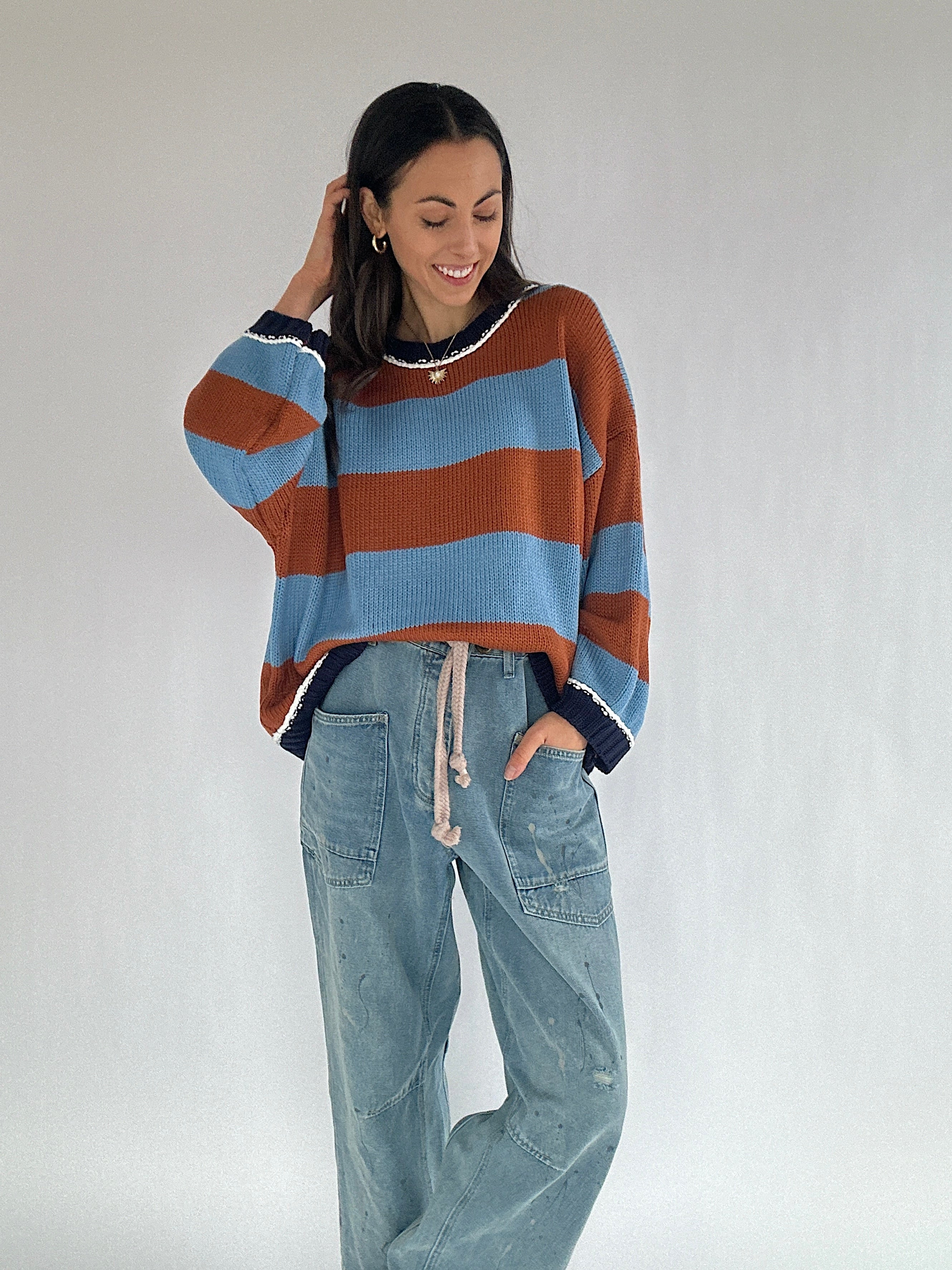 Woman wearing a brown and blue striped sweater and jeans against a plain background