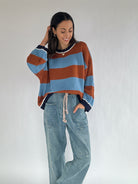Woman wearing a brown and blue striped sweater and jeans against a plain background