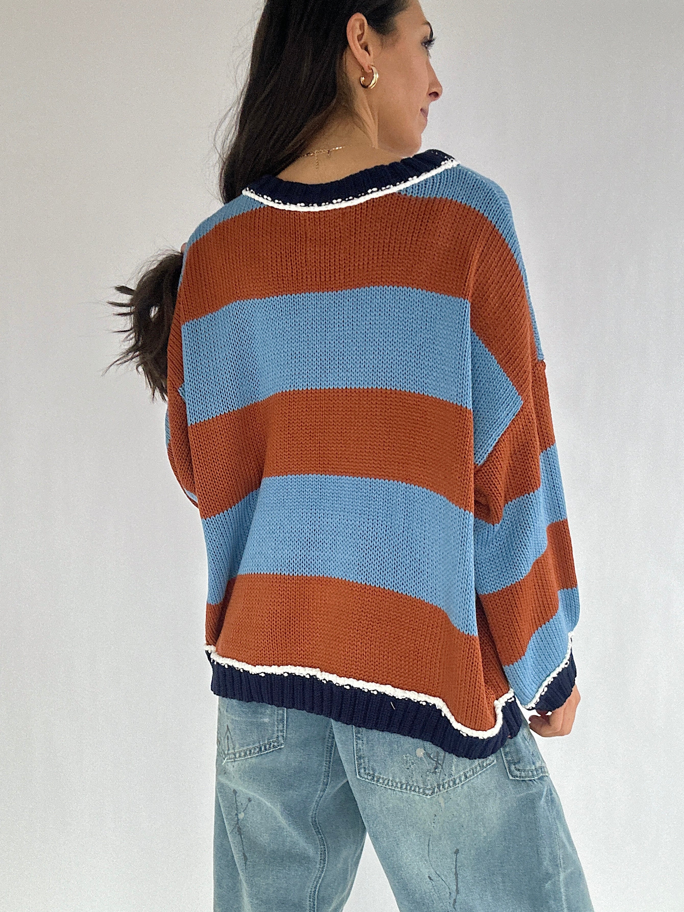 Person wearing a striped sweater with blue and brown colors on a plain background from the back
