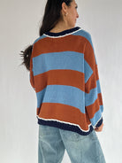 Person wearing a striped sweater with blue and brown colors on a plain background from the back