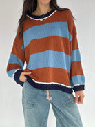 Person wearing a striped sweater with brown, blue, and navy colors on a white background
