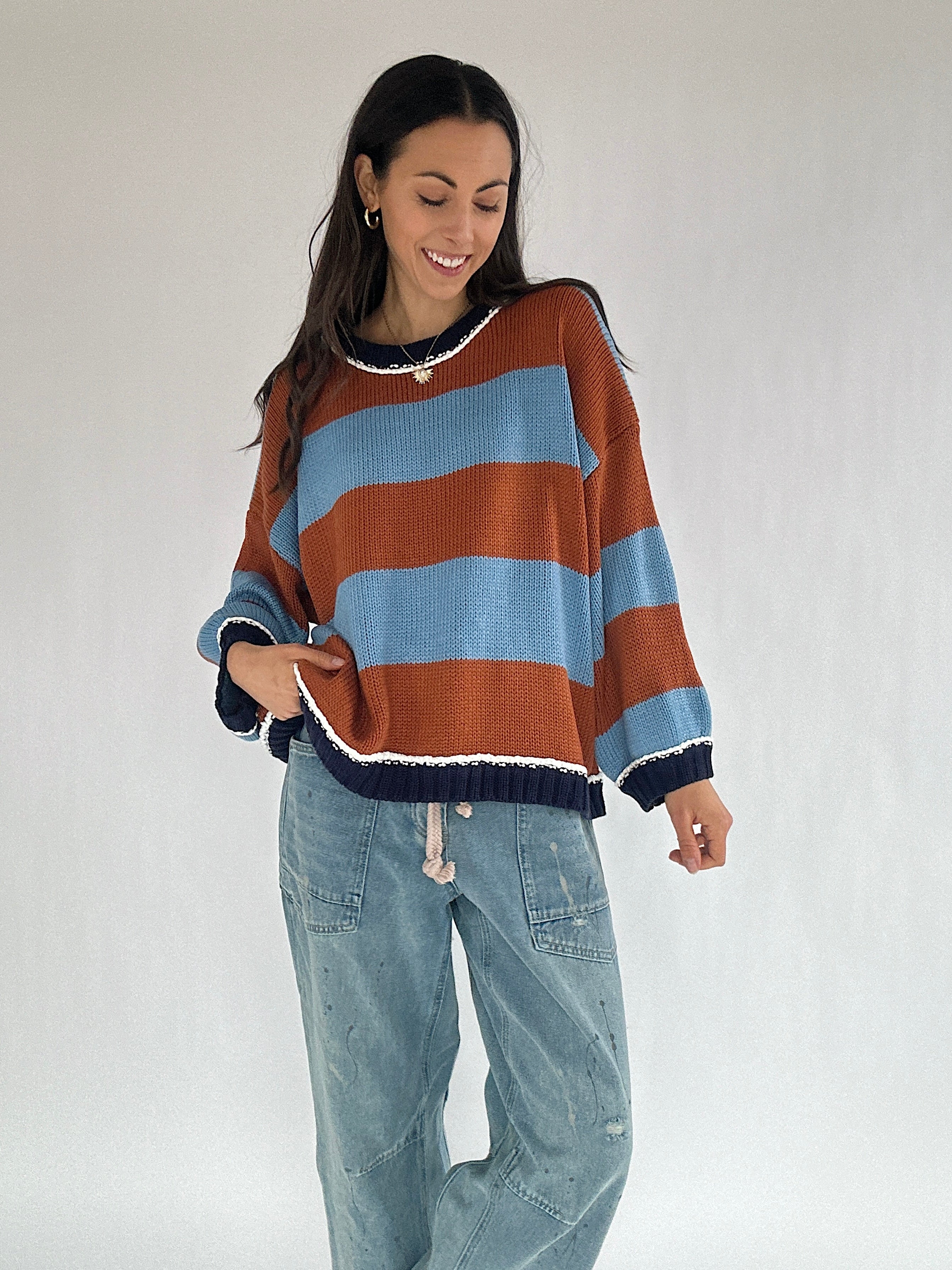 Woman wearing a blue and brown striped sweater and jeans on a plain background