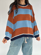 Person wearing a striped sweater with blue and brown horizontal stripes on a plain background