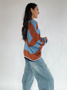 Woman wearing a brown and blue striped sweater and jeans against a plain background showing side