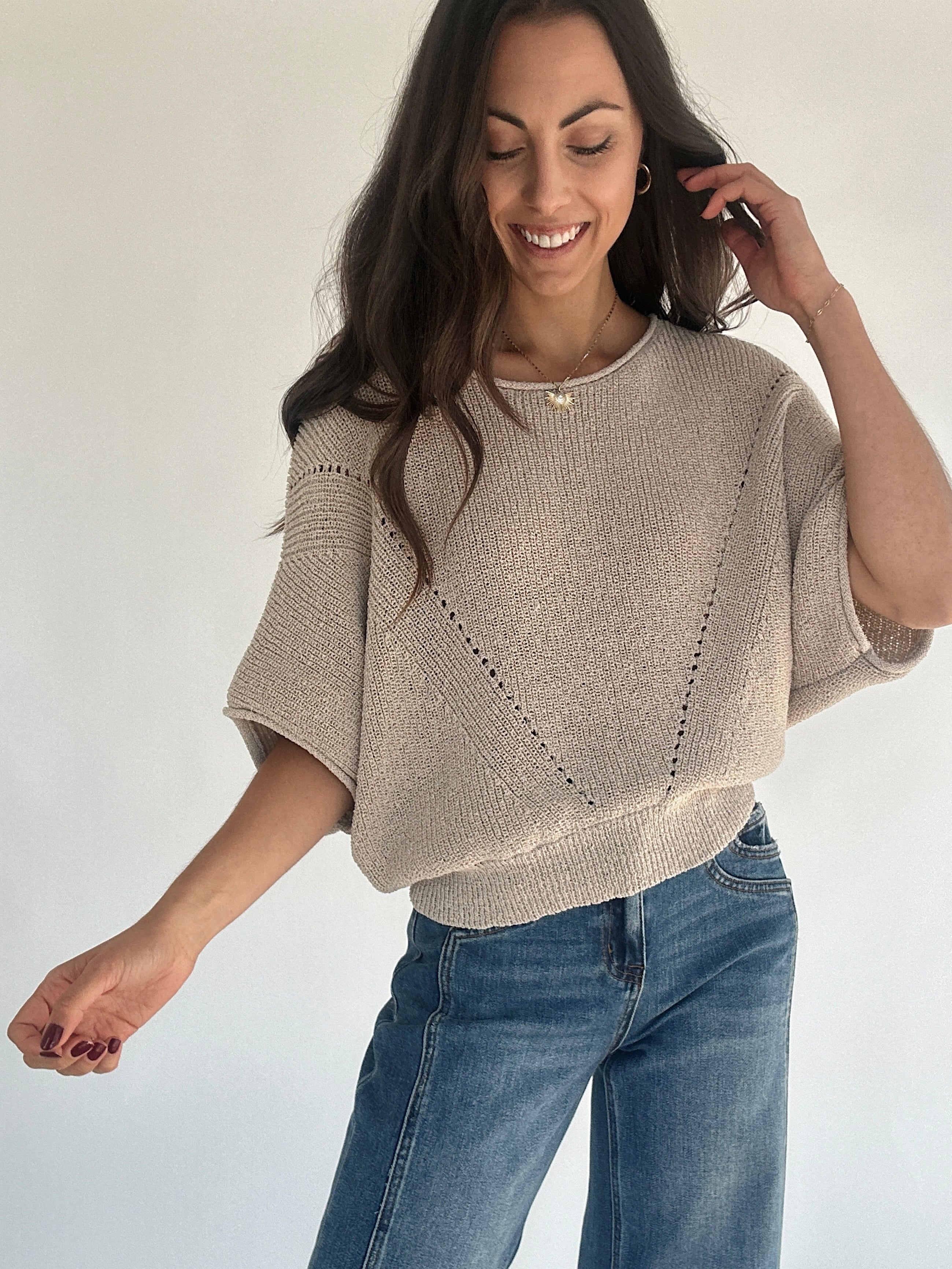 Woman wearing oatmeal knit sweater and jeans against plain background