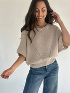 Woman wearing oatmeal knit sweater and jeans against plain background
