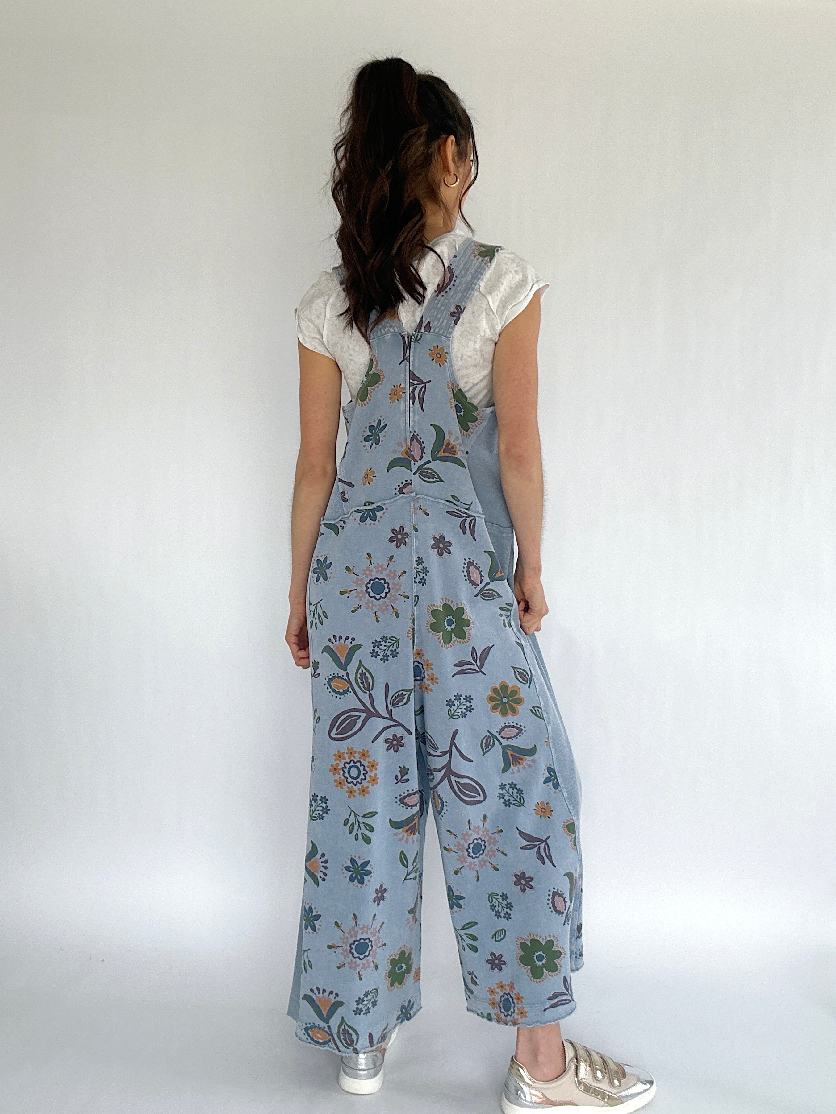 Person wearing a floral patterned blue jumpsuit against a white background showing back