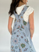Person wearing a floral blue jumpsuit over a white top against a plain background showing the back zipper detail