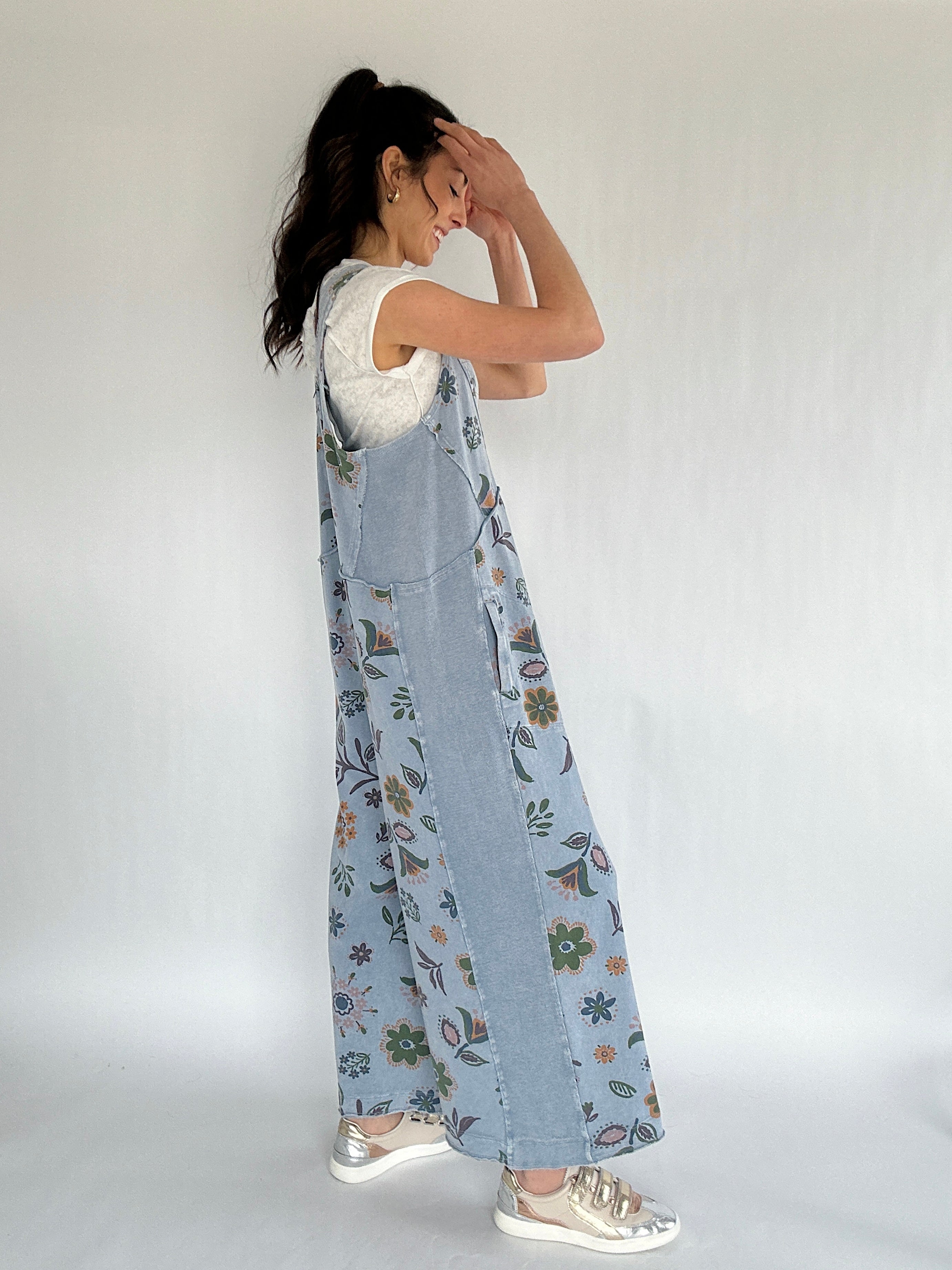 Woman wearing a floral denim jumpsuit against a white background showing side