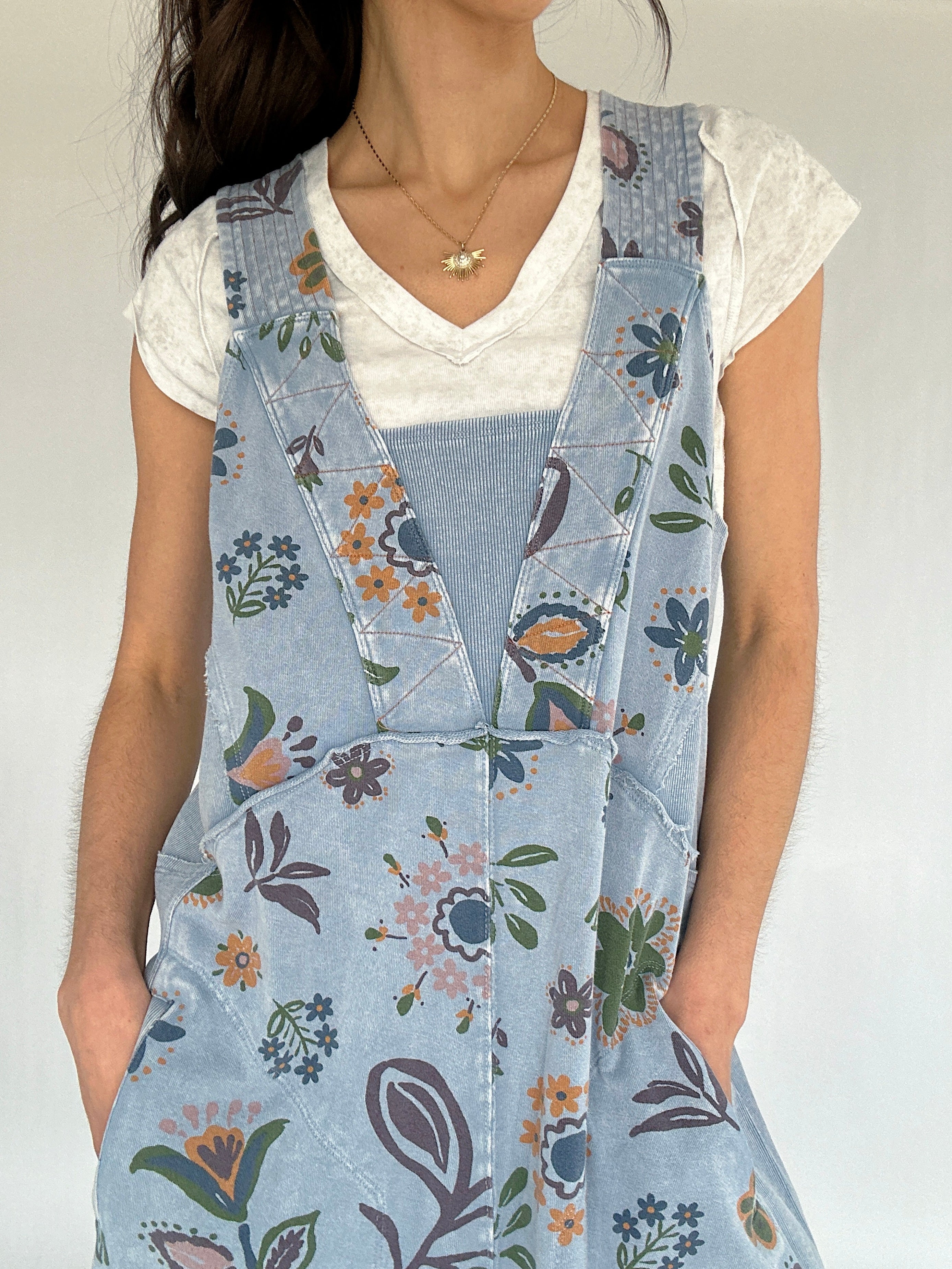 Person wearing a floral jumpsuit over a white shirt against a plain background