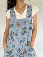 Person wearing a floral jumpsuit over a white shirt against a plain background