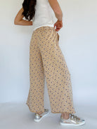 Person wearing beige floral pants and white sneakers on a plain background