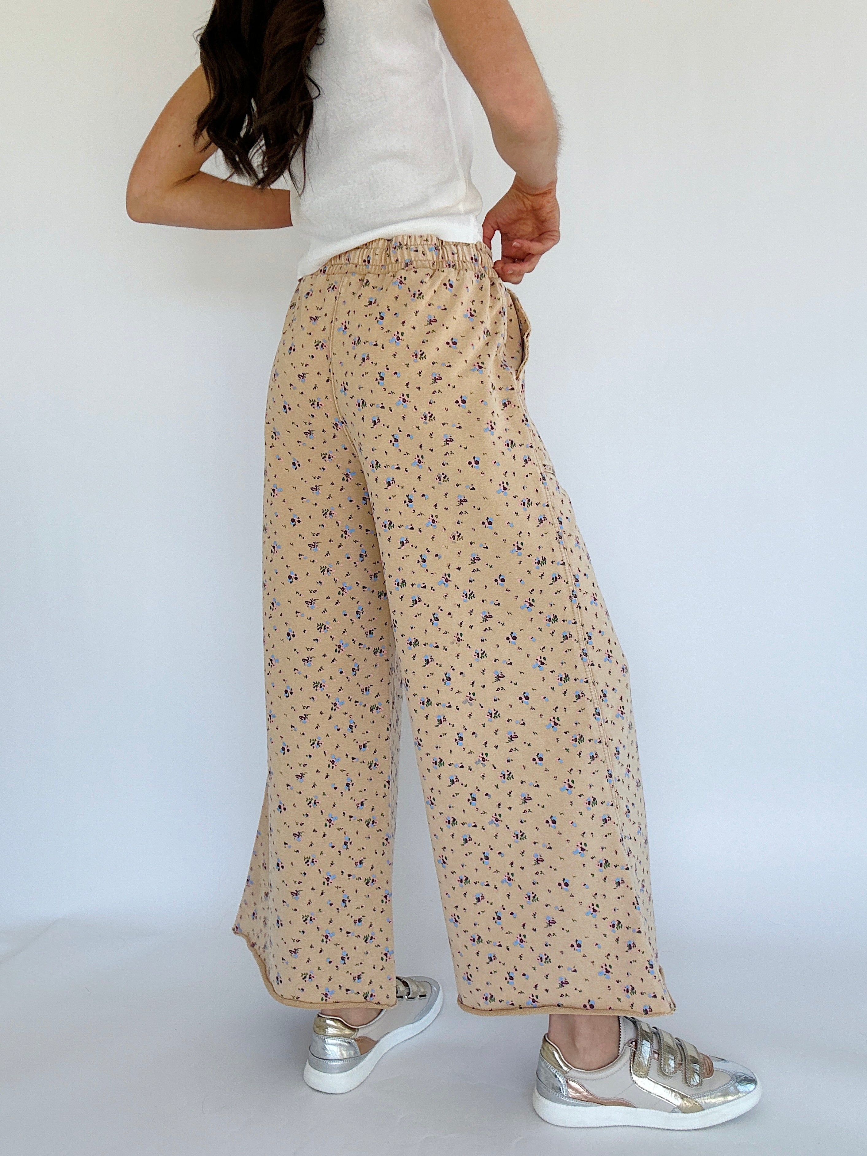 Person wearing beige floral pants and white sneakers on a plain background