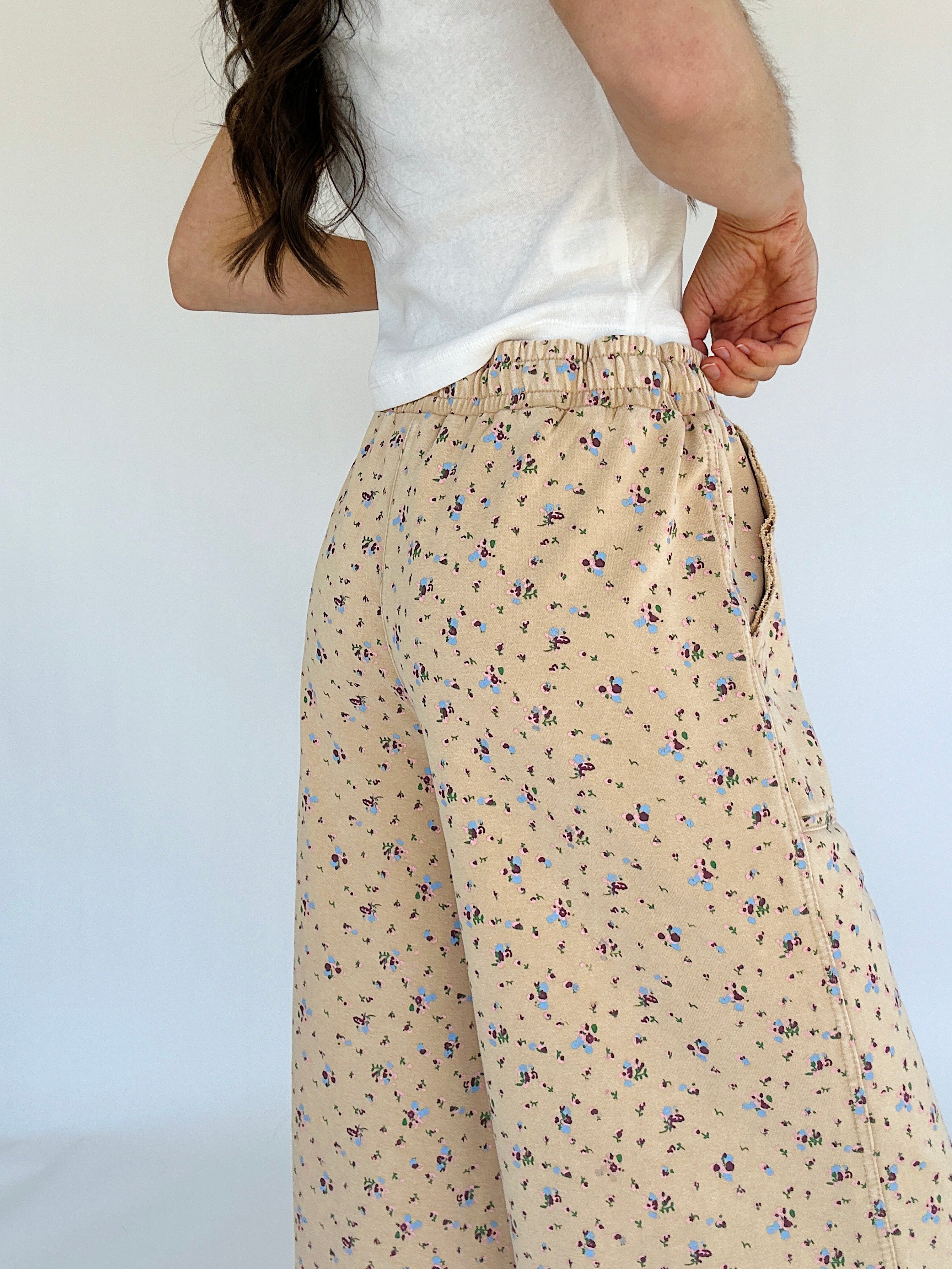 Person wearing beige floral pants with a white top against a plain background