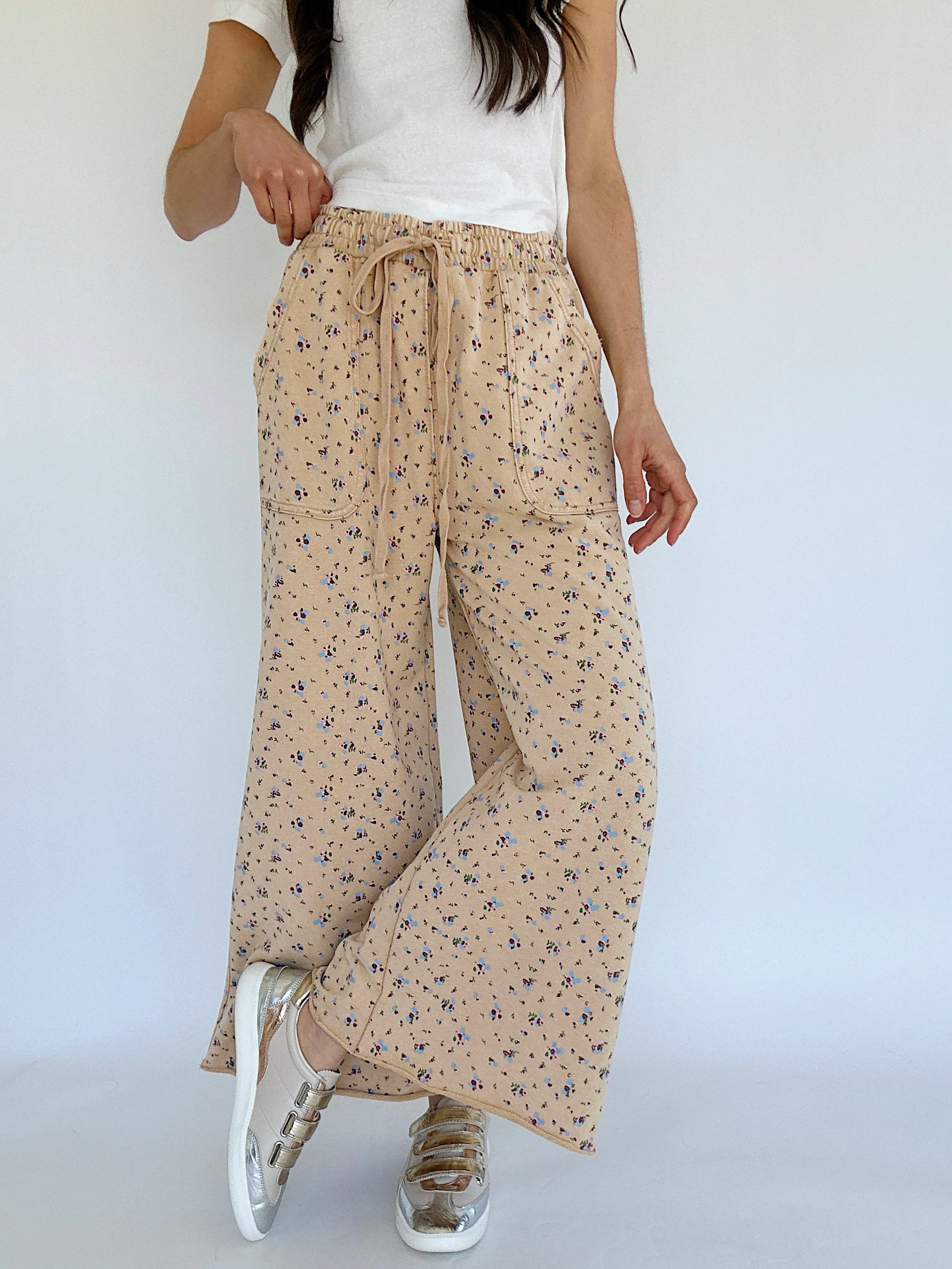 Person wearing beige floral wide-leg pants with a white top on a plain background