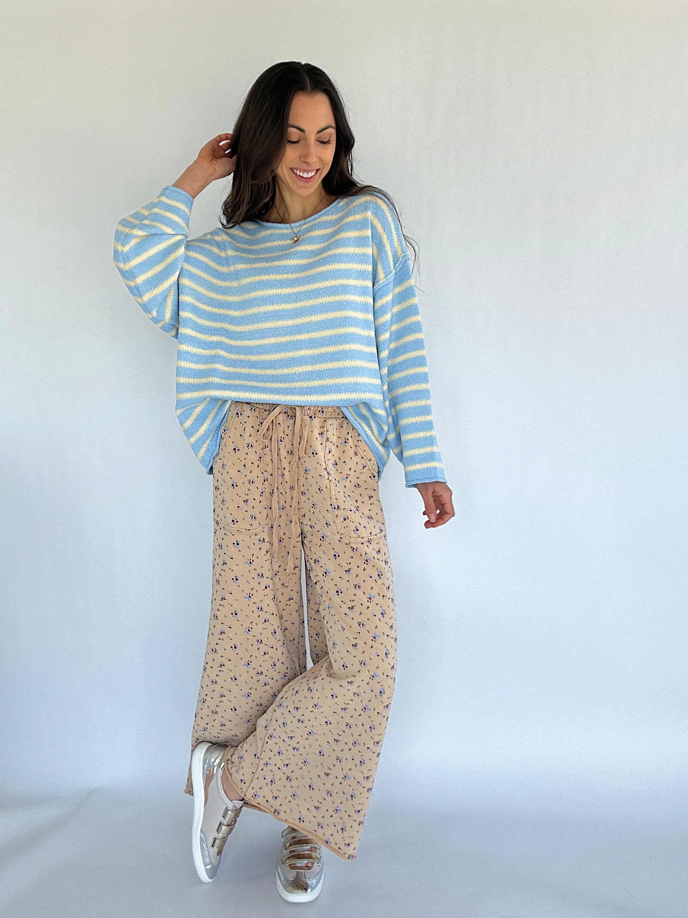 Woman wearing a striped sweater and floral patterned pants against a white background
