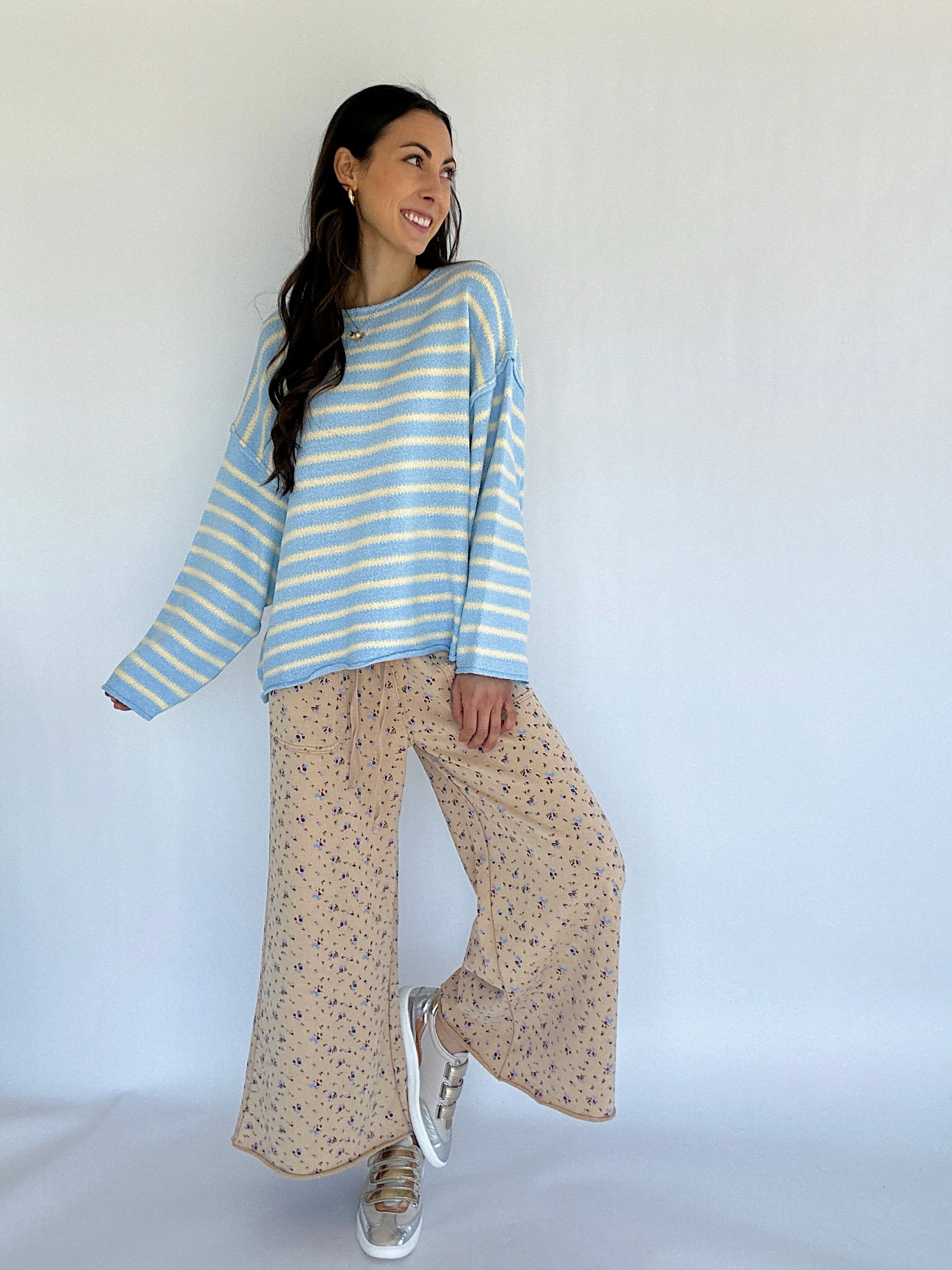 Woman wearing a blue and white striped sweater and beige patterned pants against a white background
