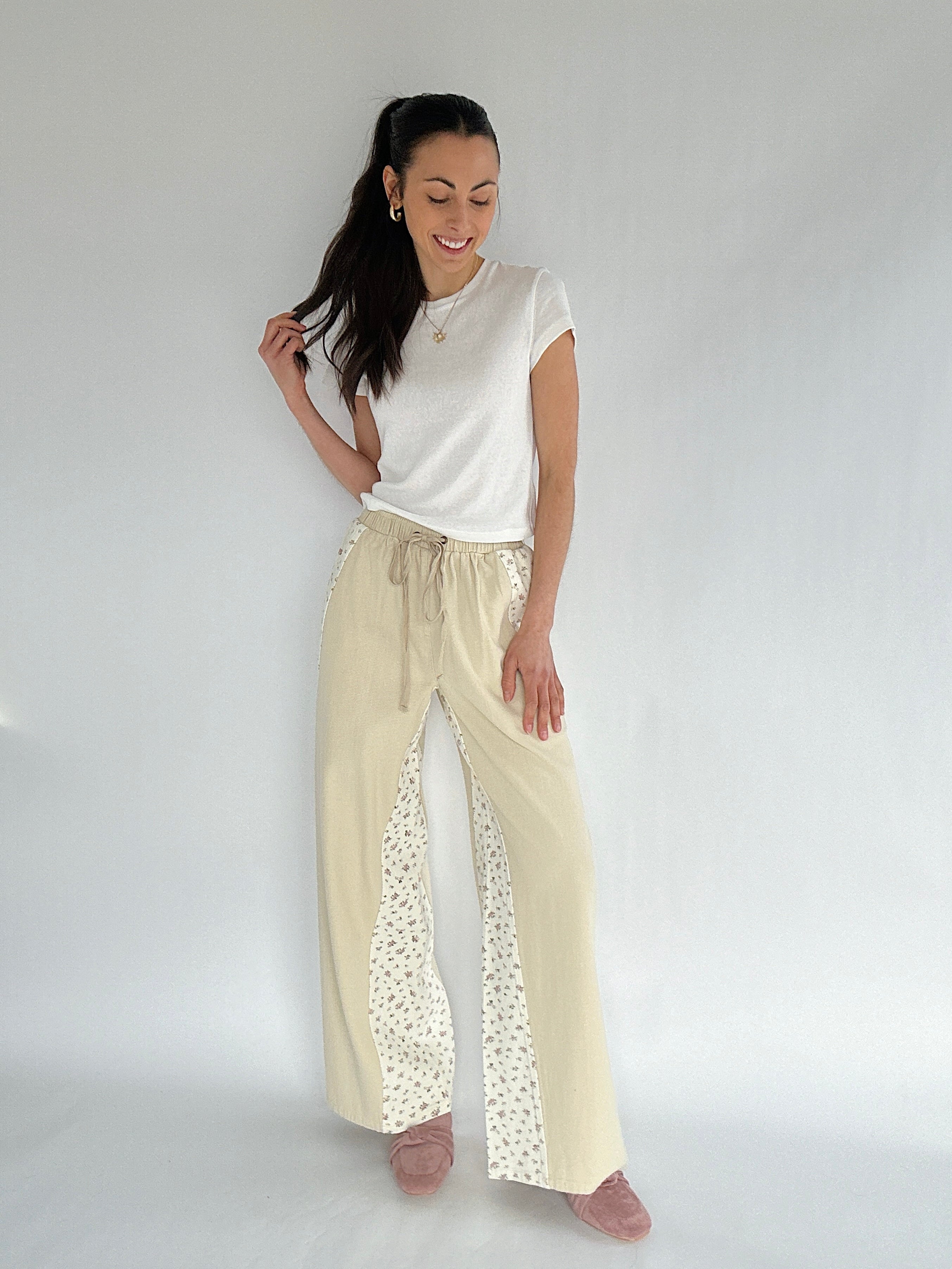 Woman wearing a white top and beige pants with floral accents on a plain background