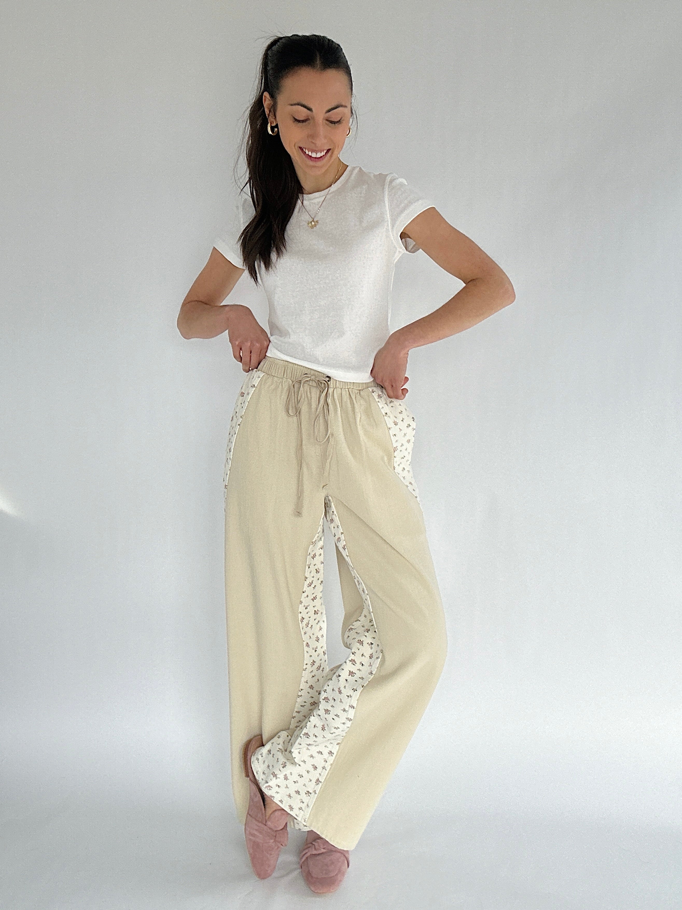 Woman wearing a white top and beige pants with floral accents on a plain background