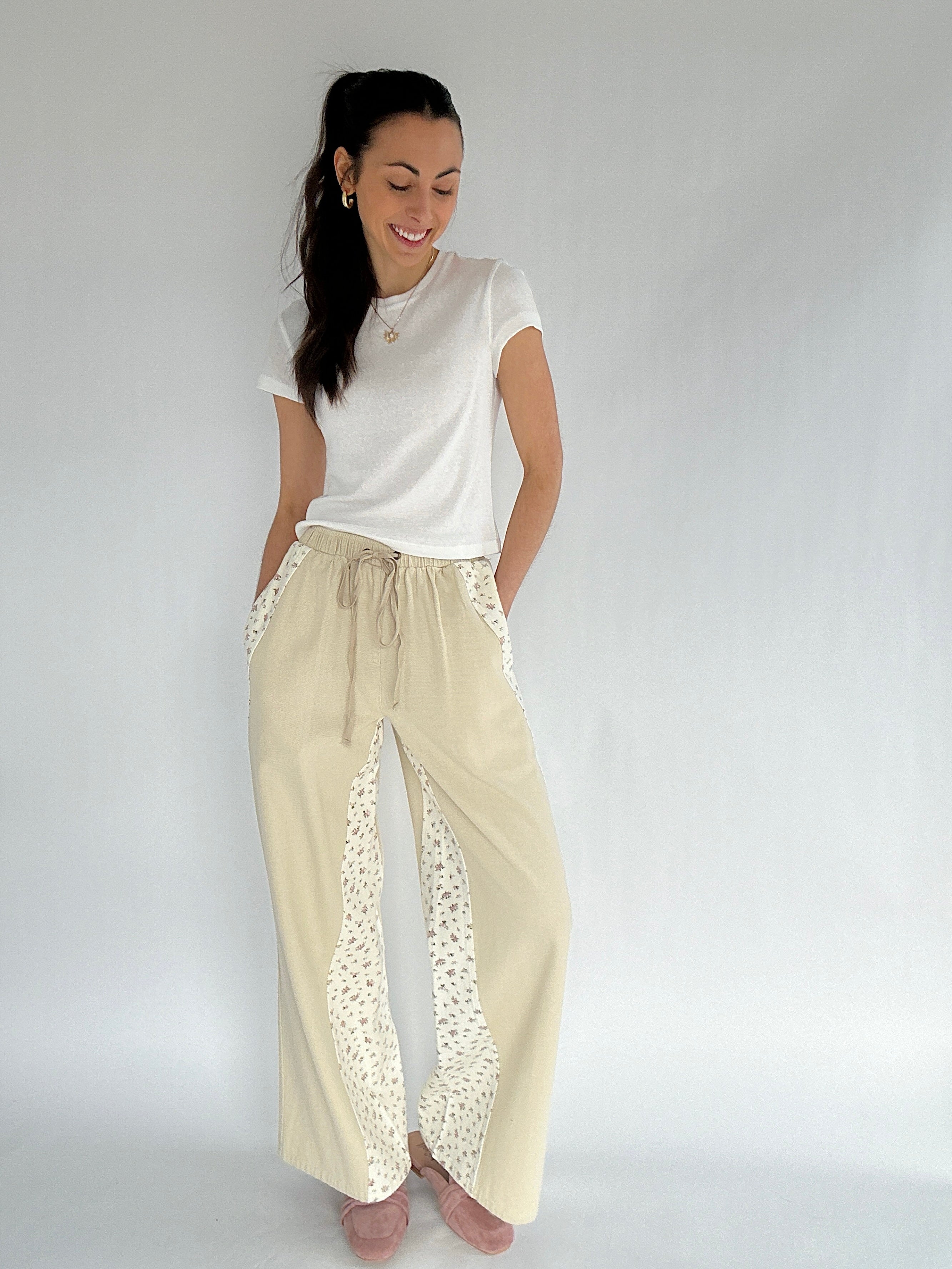 Woman wearing a white top and beige pants with floral accents on a plain background