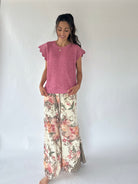 A woman modeling a pink textured short-sleeve top and wide-leg floral pants with a checkered hem, standing against a plain white studio background.