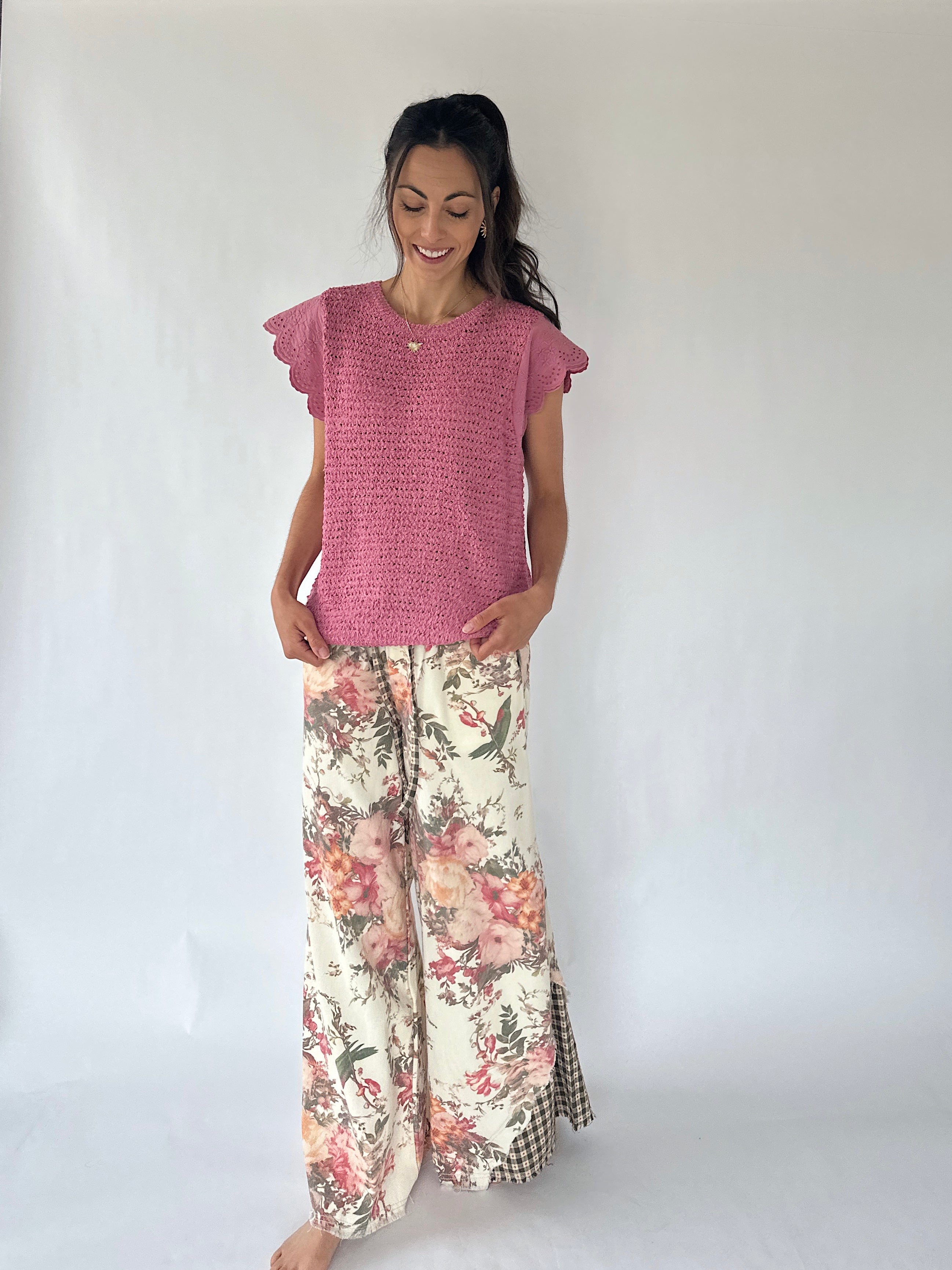 A woman modeling a pink textured short-sleeve top and wide-leg floral pants with a checkered hem, standing against a plain white studio background.