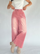 Person wearing pink corduroy pants and a white top on a plain background with legs crossed