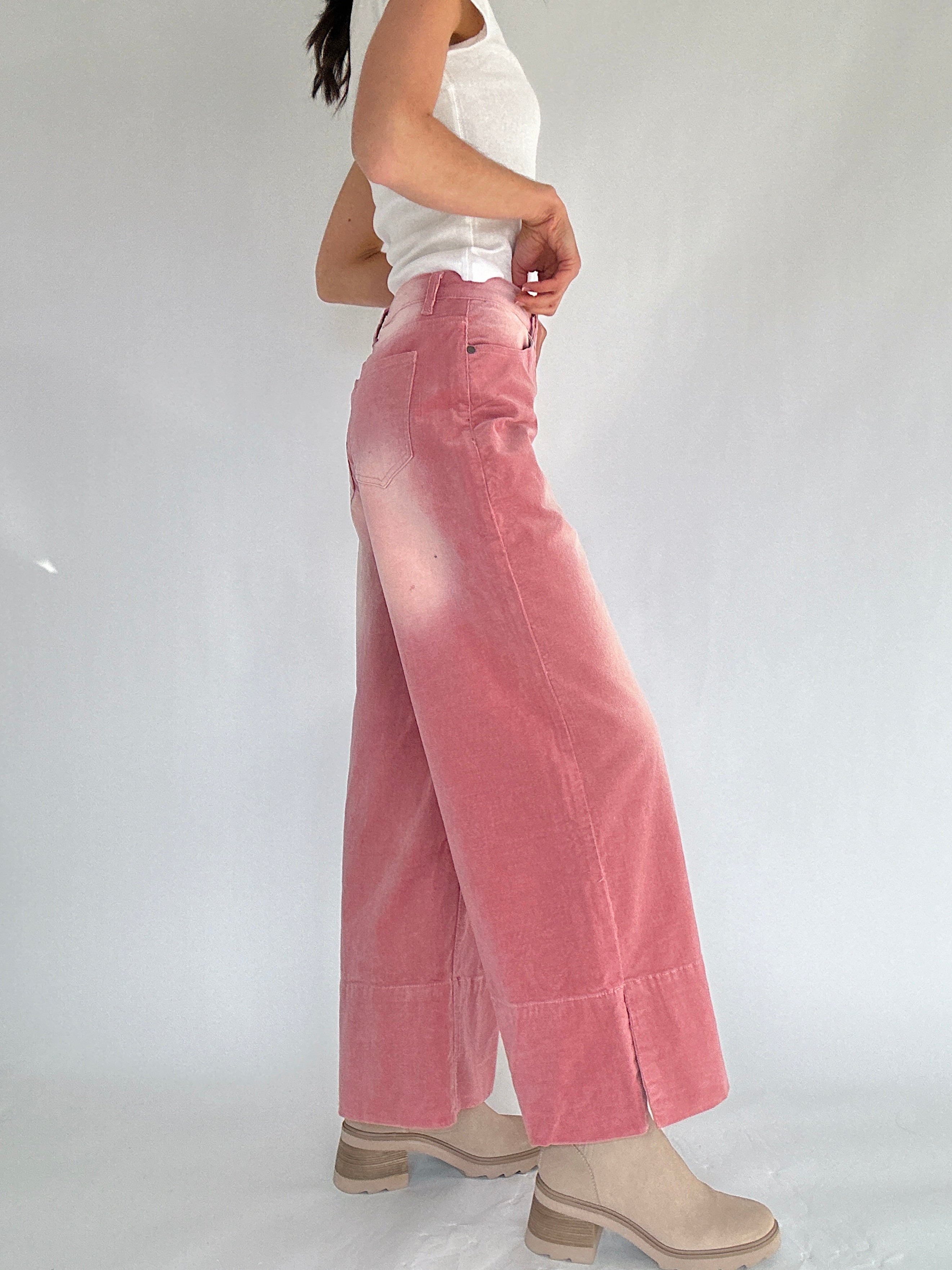 Person wearing pink corduroy wide-leg pants and a white top on a plain background from side