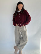 Woman wearing a burgundy cardigan and plaid barrel style pants against a white background