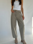 Person wearing plaid barrel pants and a white top on a plain background