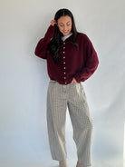 Woman wearing a burgundy sweater and plaid pants against a white background