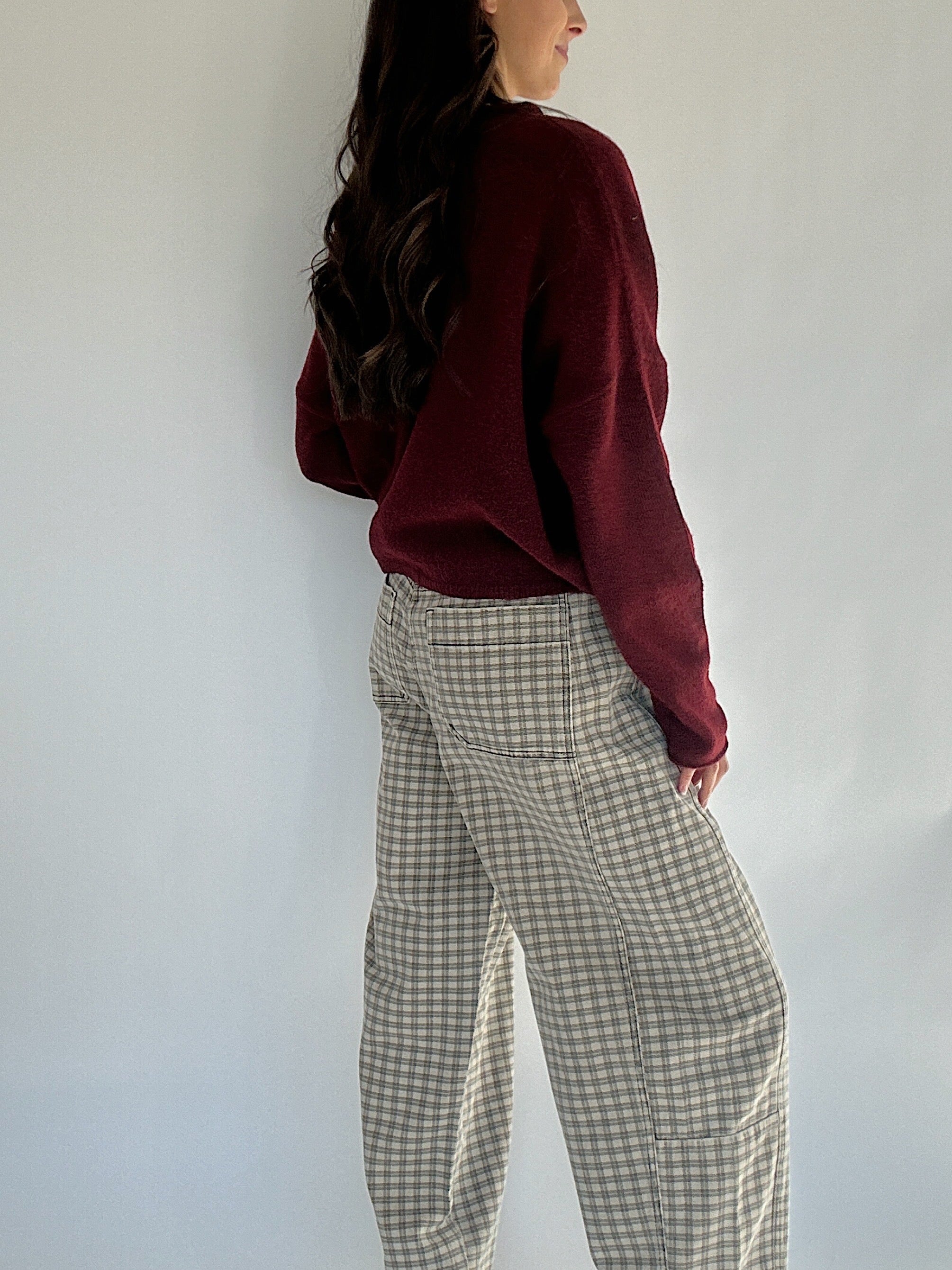 Person wearing a burgundy sweater and checkered pants against a white wall showing side view