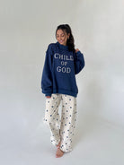 Woman wearing a navy blue sweatshirt with 'Child of God' text and white pants with black polka dots on a plain background